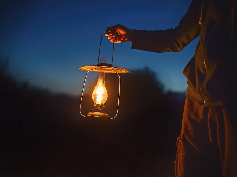 in the light of dusk, we see half of a man's outline holding a lit lantern.